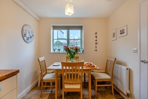 A dining area with a table set for four, a window with a view, and a radiator on the floor. - 3 Bed in Watchet (oc-c29959) (Watchet)