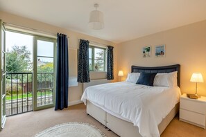 A bedroom with a bed, a nightstand, a lamp, a window with curtains, and a view of the outside. - 3 Bed in Watchet (oc-c29959) (Watchet)