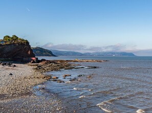 A rocky beach with a cliff, calm sea, and distant mountains. - 3 Bed in Watchet (oc-c29959) (Watchet)