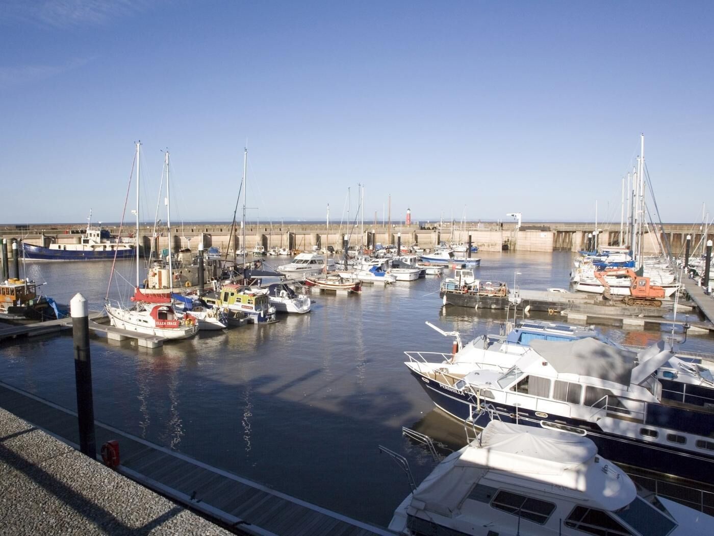 Un puerto deportivo con varias embarcaciones amarradas, cielo despejado y mar en calma.