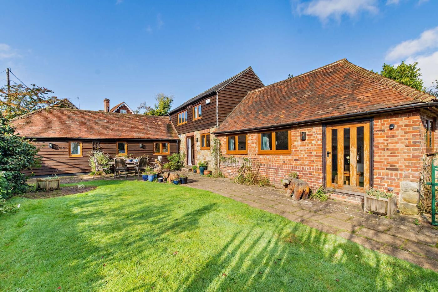 A two-story house with a brick exterior and a tiled roof. There is a small garden with a lawn and a wooden table.
