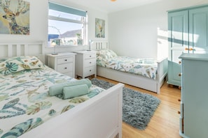 A bedroom with two beds, a nightstand, a dresser, and a window with a view.