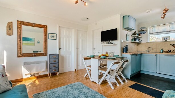 A modern kitchen with a dining area, a large mirror, and a television. - 2 Bed in Mullion (oc-k7968) (Mullion)