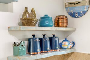 A kitchen shelf with sugar, coffee, and tea containers, a decorative teapot, and a wall clock.