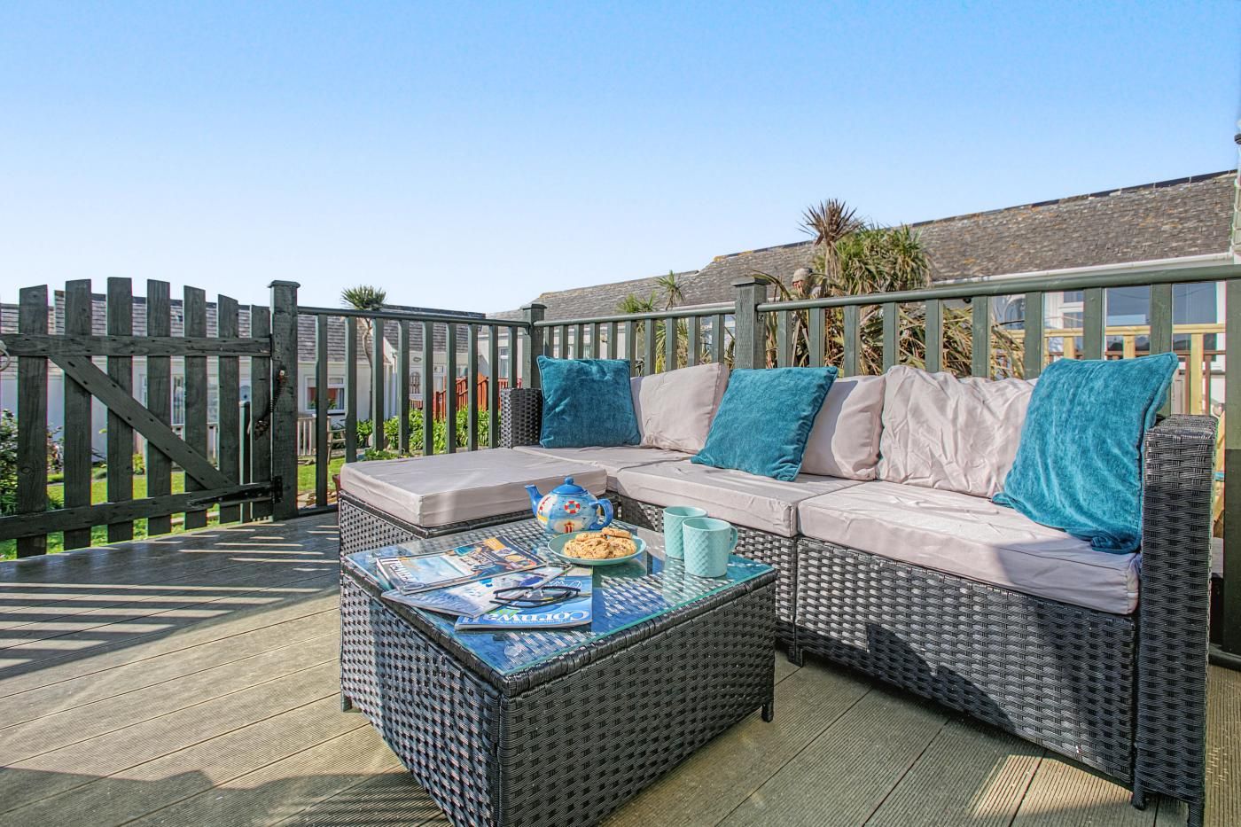 A wicker sofa with cushions, a table with magazines, and a teapot.