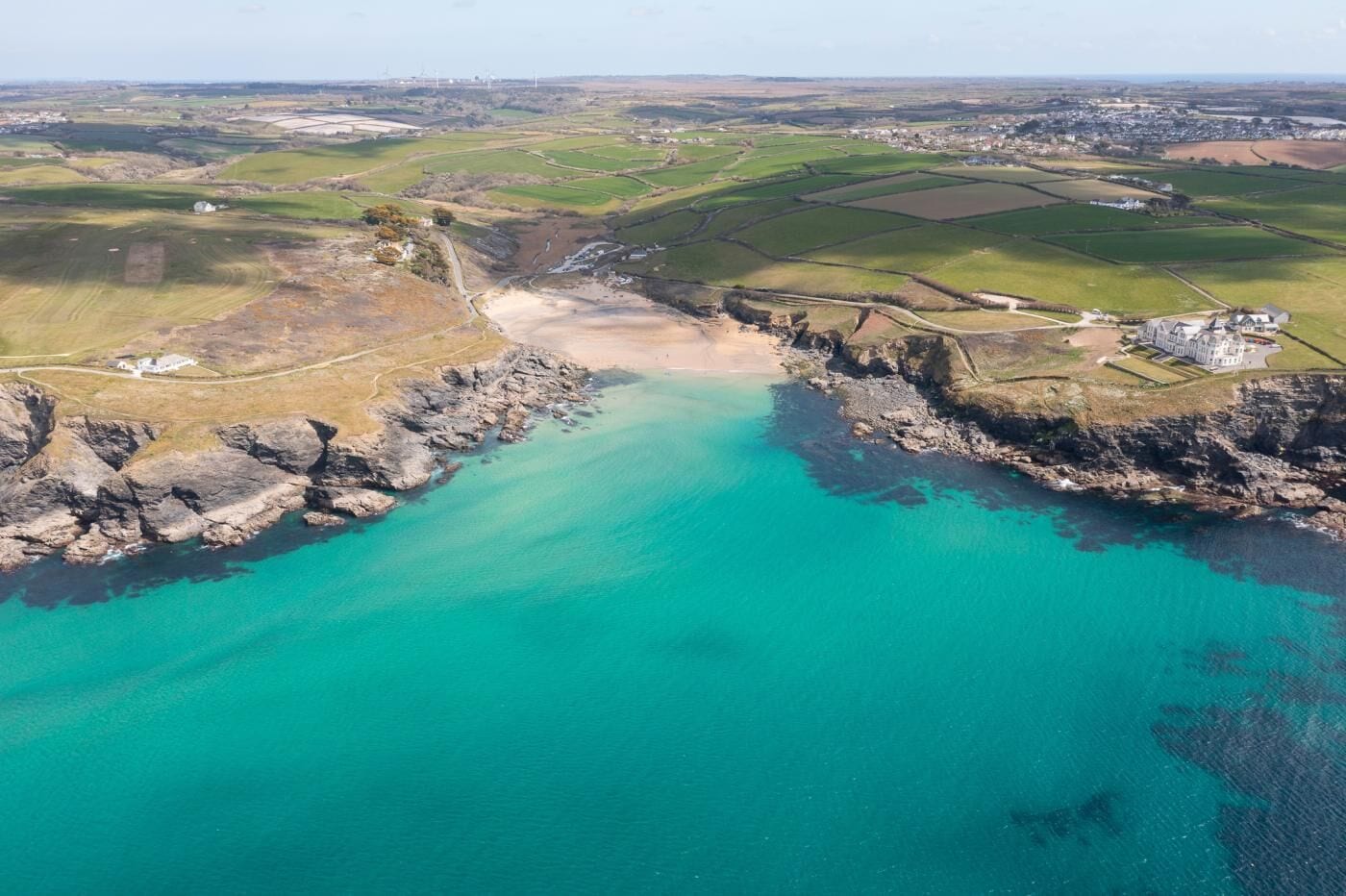 An aerial view of a coastal area with a large body of turquoise water, rocky cliffs, and a distant town.