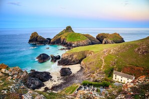 A coastal landscape with rocky outcrops, a sandy beach, and a white building with a garden.