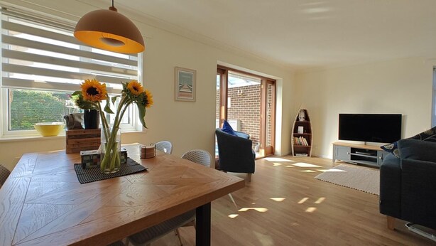 Una sala de estar moderna con una mesa de comedor de madera, un sofá, un televisor y una estantería.