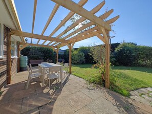 A wooden pergola structure with a table and chairs underneath, set in a garden with a grassy lawn and dense shrubbery. - 2 Bed in Norton (oc-l30264) (Freshwater)