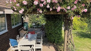 Un área de patio al aire libre con una mesa y sillas, rodeada de exuberante follaje y plantas en flor.