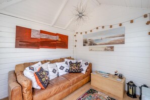 A room with a brown leather sofa, a wooden nightstand, and a painting of a beach scene.