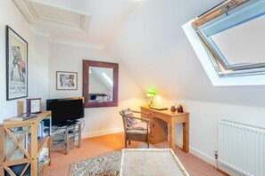 A room with a television, desk, chair, and a window with a view.