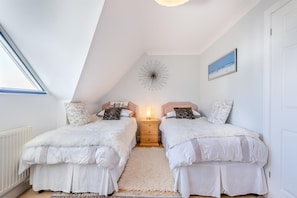 A bedroom with two beds, a ceiling light, a radiator, and a window.