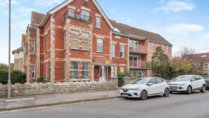 En flereetagers boligbygning med murstensfacade, adskillige vinduer og en stenvæg foran.
