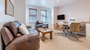 En moderne stue med en lædersofa, en lænestol, et spisebord med stole og et fladskærms-tv på væggen.