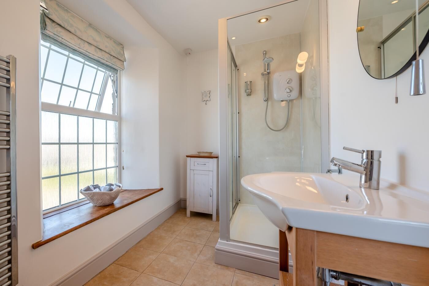 A bathroom with a shower, a sink, a window with a view, and a towel rack.