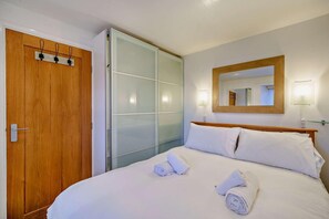 Ein Hotelzimmer mit Holztür, Schiebetüren zum Kleiderschrank, einem Bett mit weißer Bettwäsche und einem Spiegel an der Wand.