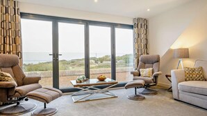 A modern living room with a large sliding glass door leading to a balcony, furnished with a sofa, two armchairs, and a coffee table. - 3 Bed in Totland Bay (oc-s30266) (Totland)