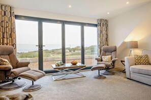 Ein modernes Wohnzimmer mit einem großen Schiebeglastür, die auf einen Balkon führt, ausgestattet mit einer Couch, zwei Sesseln und einem Couchtisch.
