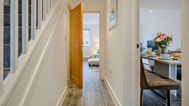 A hallway with a staircase, a wooden door, a dining area with a table set for breakfast, and a bed in the background. - 3 Bed in Totland Bay (oc-s30266) (Totland)