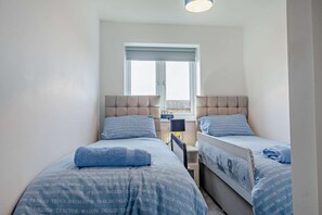 Ein Schlafzimmer mit zwei Betten, jeweils mit Kopfteil und Fenster. Ein kleiner Tisch steht zwischen den Betten.