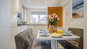 A modern kitchen with a dining area, featuring a table set for breakfast with bowls, plates, and a fruit bowl. - 3 Bed in Totland Bay (oc-s30266) (Totland)