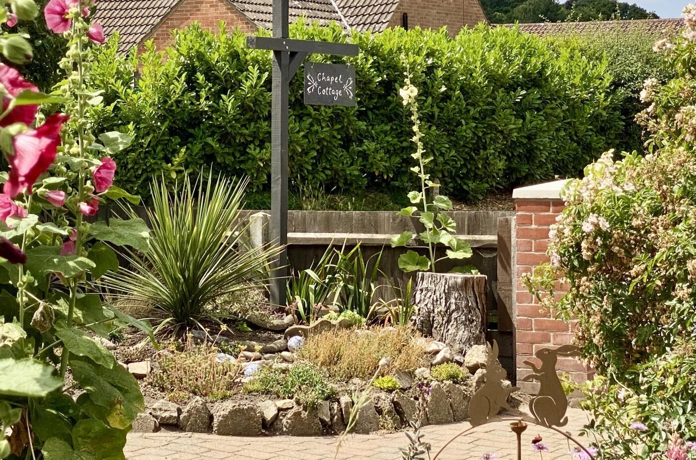 Un jardin agrémenté d’une pancarte indiquant « Chapel Cottage », entouré de diverses plantes et bordé d’un mur de pierres rustiques.
