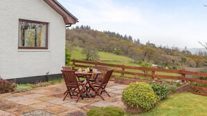 Eine Terrasse mit Tisch und Stühlen, Blick auf eine Hügellandschaft und ein Holzzaun.