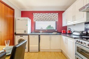 A compact kitchen with a washing machine, a toaster, and a red kettle. - 2 Bed in Ardvasar (oc-l30278) (Ardvasar)