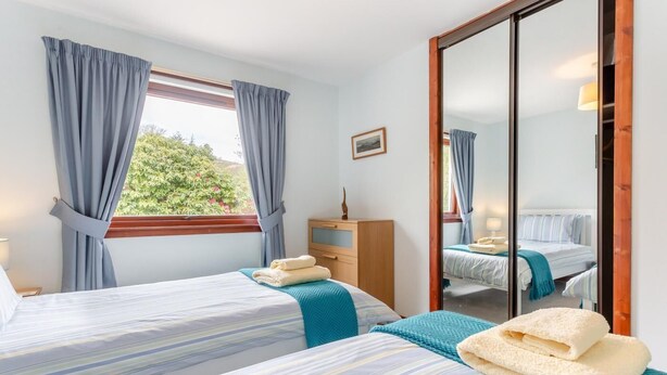 Ein Schlafzimmer mit zwei Betten, einer hölzernen Kommode, einem Spiegel und einem Fenster mit Vorhängen.