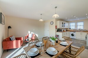 Une cuisine moderne avec des meubles blancs, un lave-linge et un coin repas doté d’une table en bois, mise pour quatre personnes.