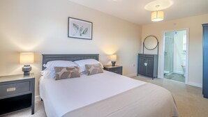 Quarto com cama, duas mesas de cabeceira com luminárias, guarda-roupa e porta do banheiro.