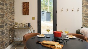 Ein Essbereich mit einer Steinswand, einem Holzkunstwerk, einem roten Topf, Weingläsern und einem Brot auf dem Tisch.