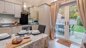 A compact kitchen with modern appliances, a dining area with a table set for two, and a sliding glass door leading to an outdoor patio. - 3 Bed in Wilberfoss (oc-t30301) (Wilberfoss)