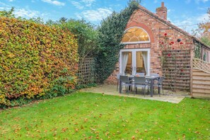 A brick house with a covered patio, a wooden fence, and a well-maintained garden. - 3 Bed in Wilberfoss (oc-t30301) (Wilberfoss)