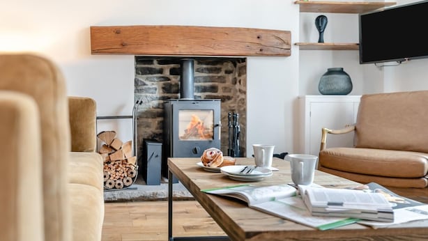 Ein gemütliches Wohnzimmer mit Kamin aus Stein, einer Couch, einem Tisch mit Frühstücksgebäck und einem Fernseher an der Wand.
