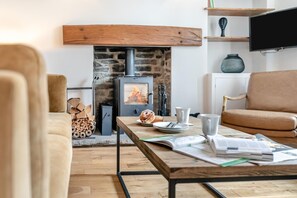 Ein gemütliches Wohnzimmer mit Kamin aus Stein, einer Couch, einem Tisch mit Frühstücksgebäck und einem Fernseher an der Wand.