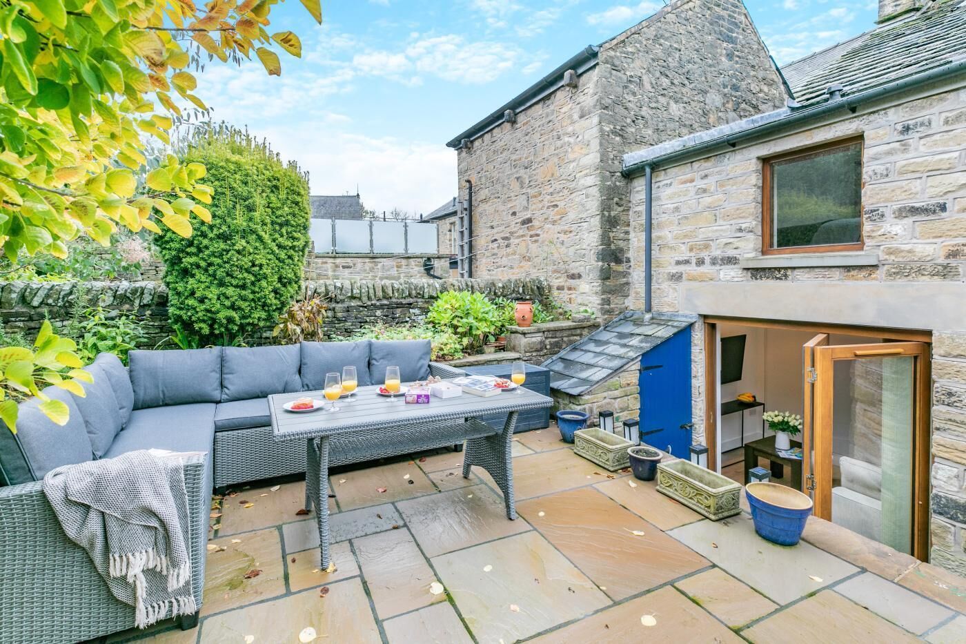 A stone building with a blue door, a grey sofa, and a table with drinks and snacks.