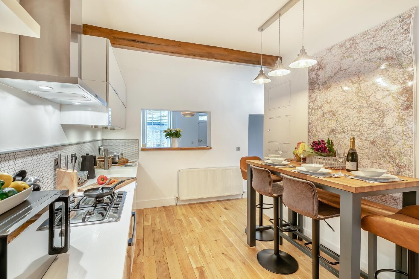 A modern kitchen with a central island, wooden ceiling beams, and a dining area with bar stools.