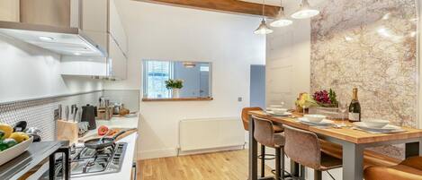 A modern kitchen with a central island, wooden ceiling beams, and a dining area with bar stools.