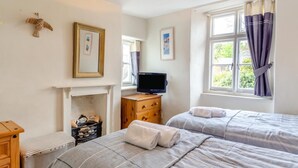 A bedroom with two beds, a television, a fireplace, and a window with curtains. - 3 Bed in Thurlestone (oc-h30263) (Thurlestone Sands)