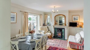 A dining area with a table set for four, a fireplace, a television, and a sofa in a well-lit room with natural light. - 3 Bed in Thurlestone (oc-h30263) (Thurlestone Sands)