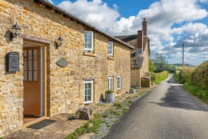 A stone building with a wooden door, a small window, and a sign reading 'The Old Cottage.'