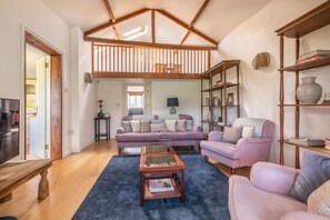 A living room with a high ceiling, wooden beams, a sofa set, a coffee table, and a bookshelf. - 3 Bed in Beaminster (oc-t30165) (Beaminster)