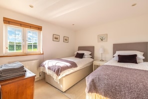 A bedroom with two beds, a window, a radiator, and a desk with towels. - 3 Bed in Beaminster (oc-t30165) (Beaminster)