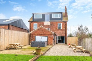 Une maison à deux étages avec un garage, une terrasse dotée de tables de pique-nique et un jardin.