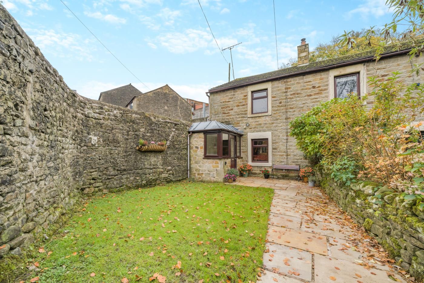 A stone wall, a grassy yard, and a stone pathway leading to a building with a window and a door.
