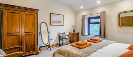 A bedroom with a bed, a wooden wardrobe, a mirror, a chair, and a window with curtains.