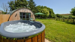 Ein Whirlpool vor einem Holzbau mit Glastür, umgeben von einer grünen Wiese und Bäumen.