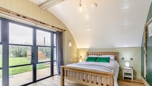 Ein Schlafzimmer mit einem Holzbett, einem Nachttisch, einer Lampe und Blick auf den Garten durch große Schiebetüren.